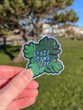 Hand holding a sticker with 'Crazy Plant Lady' text against a blurred outdoor background